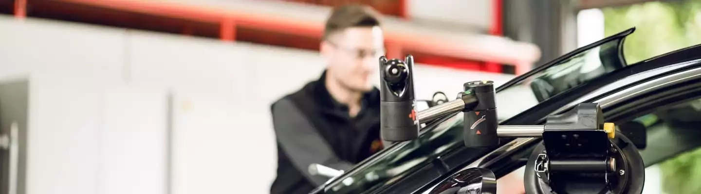 Monteur bedient Gerätschaft an einem Auto um die Frontscheibe einzusetzen