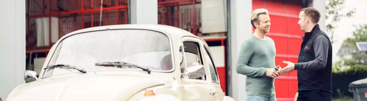Kunde und Mitarbeiter reden vor einem Oldtimer-Auto