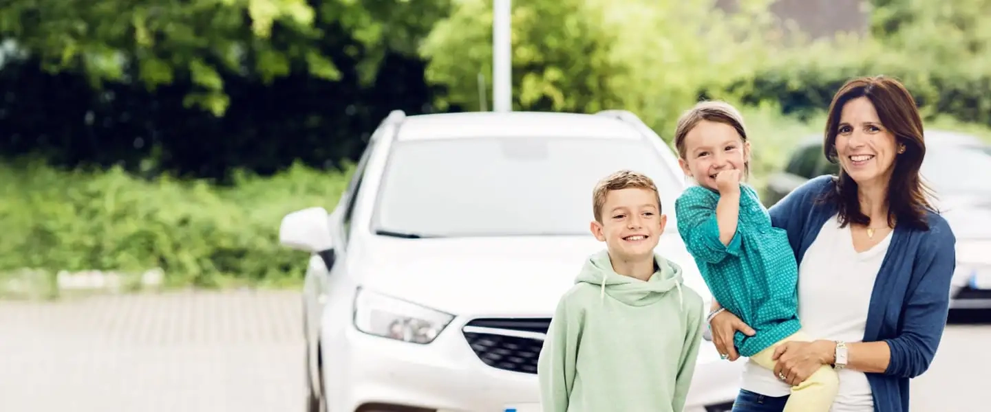 Frau mit zwei Kindern steht vor einem Auto im Freien