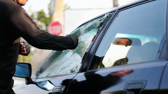 Eine Faust die eine Seitenscheibe an einem Auto einschlägt