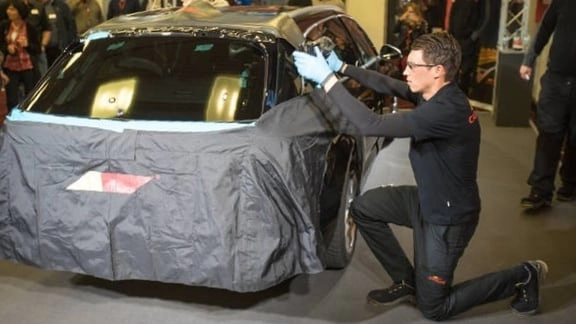 Ein junger Mann kniet vor einem Auto an dem er arbeitet. Das Auto hat eine Carglass-Schutzfolie auf.