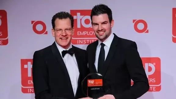 Zwei Männer stehen vor einer Fotowand mit einem Award in der Hand wo "Top Employer" drauf steht.