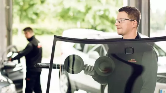 Ein Monteur, der eine Windschutzscheibe zum Auto trägt