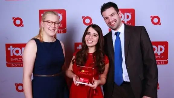 Drei lachende Menschen, die Mittlere hält einen Award mit der Aufschrift "Top Employer" in der Hand 