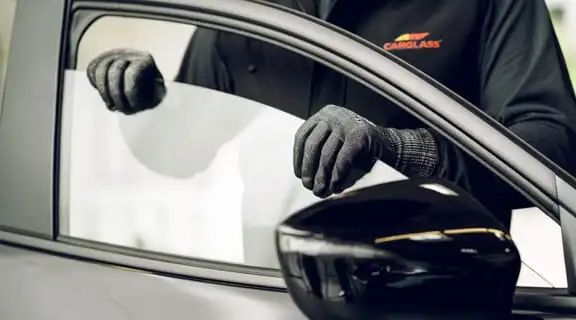 Zwei schwarze Handschuhe setzen eine Seitenscheibe in ein Auto ein