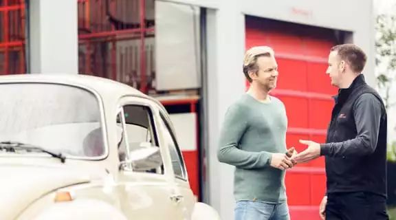 Kunde und Mitarbeiter reden vor einem Oldtimer-Auto
