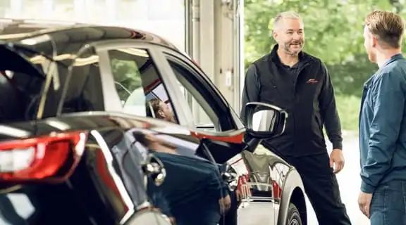Kunde und Monteur stehen neben einem Auto und reden