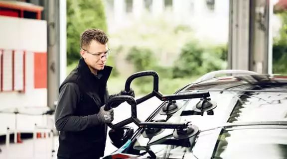 Monteur setzt mit Gerät neue Frontscheibe in Auto ein