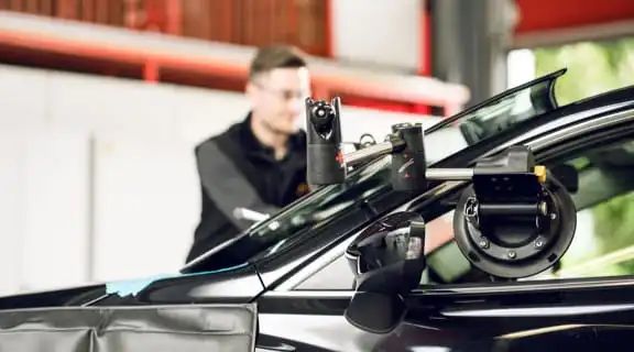 Monteur bedient Gerätschaft an einem Auto um die Frontscheibe einzusetzen