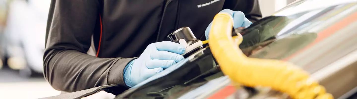 Gerät mit Schlauch, dass an einer Scheibe hängt, wird von Händen in blauen Handschuhen bedient