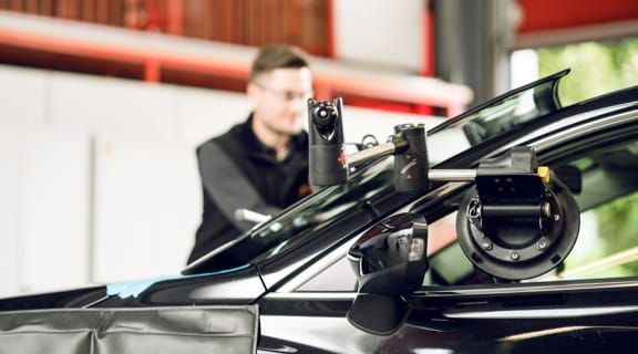 Monteur bedient Gerätschaft an einem Auto um die Frontscheibe einzusetzen