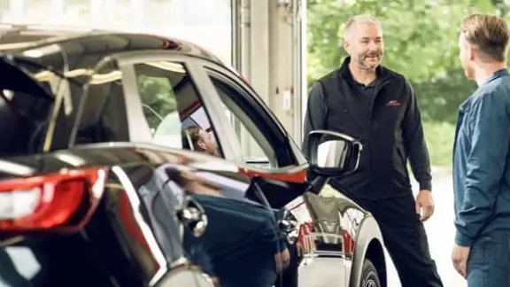 Mitarbeiter und Kunde stehen neben Fahrzeug und unterhalten sich