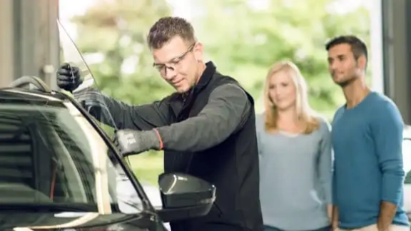 Mitarbeiter setzt Seitenscheibe im Fahrzeug ein ud Kunden schauen zu