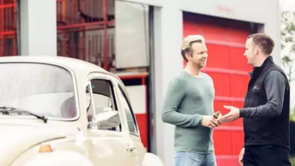 Kunde spricht mit Mitarbeiter neben Oldtimer